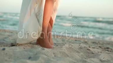 一个穿着白色长裙的白种人女孩的腿<strong>站在</strong>蔚蓝的大海的岸边，<strong>站在</strong>沙滩<strong>上</strong>，太阳，镜头.. 慢慢